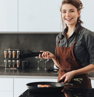 Uśmiechnięta młoda kobieta smażąca obiad na patelni w nowoczesnej kuchni