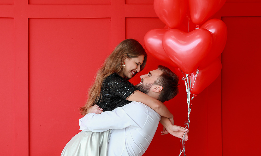 Zakochana para z czerwonymi balonami-serduszko na czerwonym tle