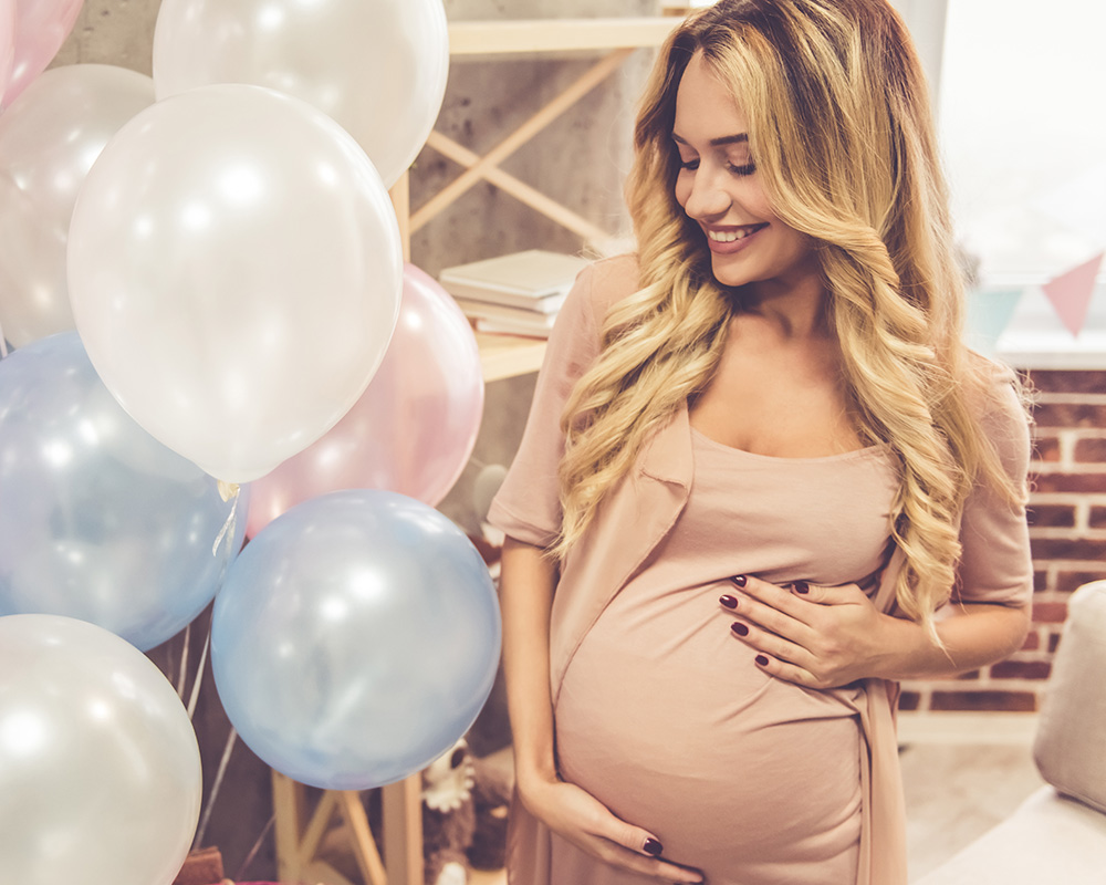Kobieta w ciąży z uśmiechem spogląda na kolorowe balony na baby shower