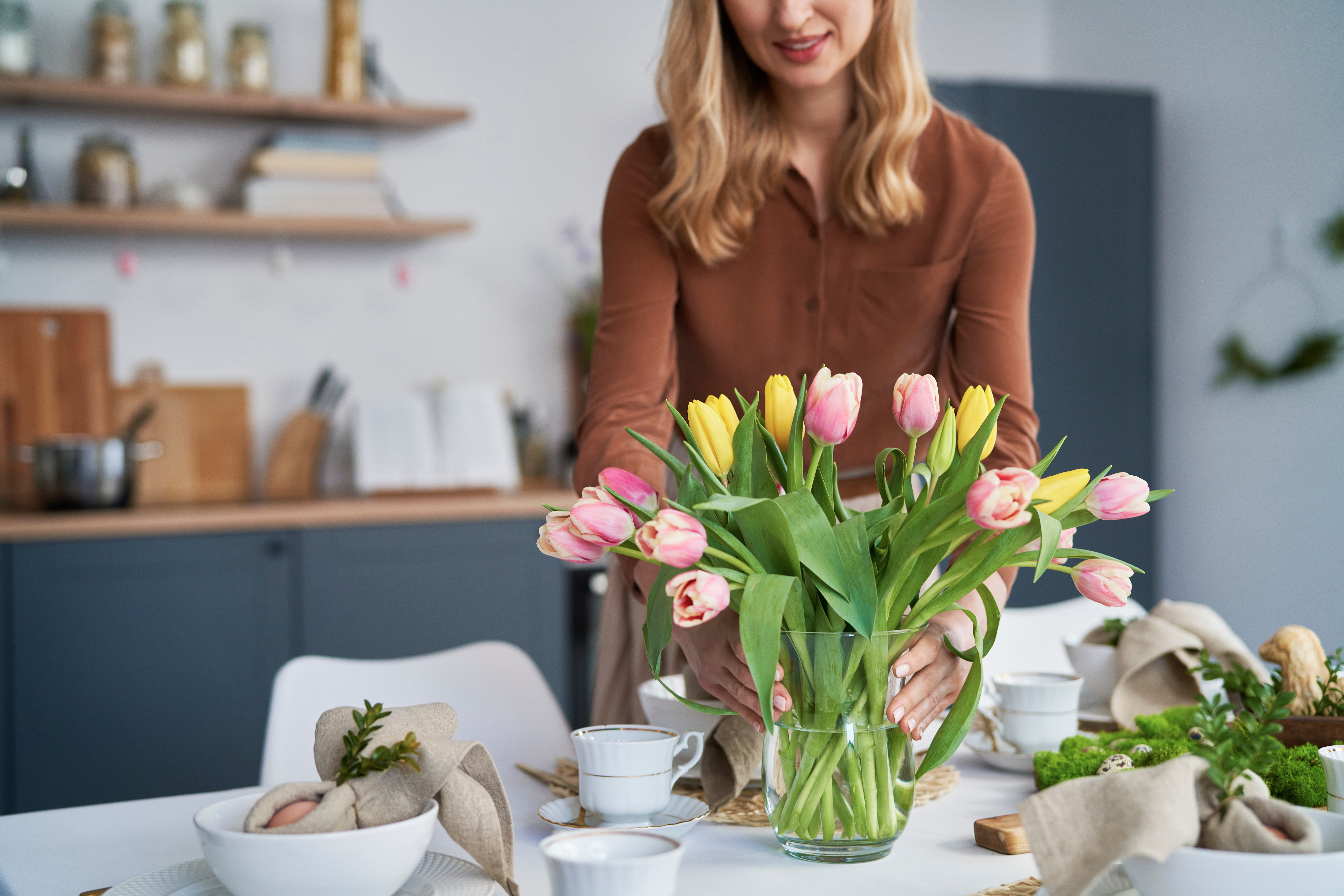 Kobieta wkłada tulipany do wazonu w salonie