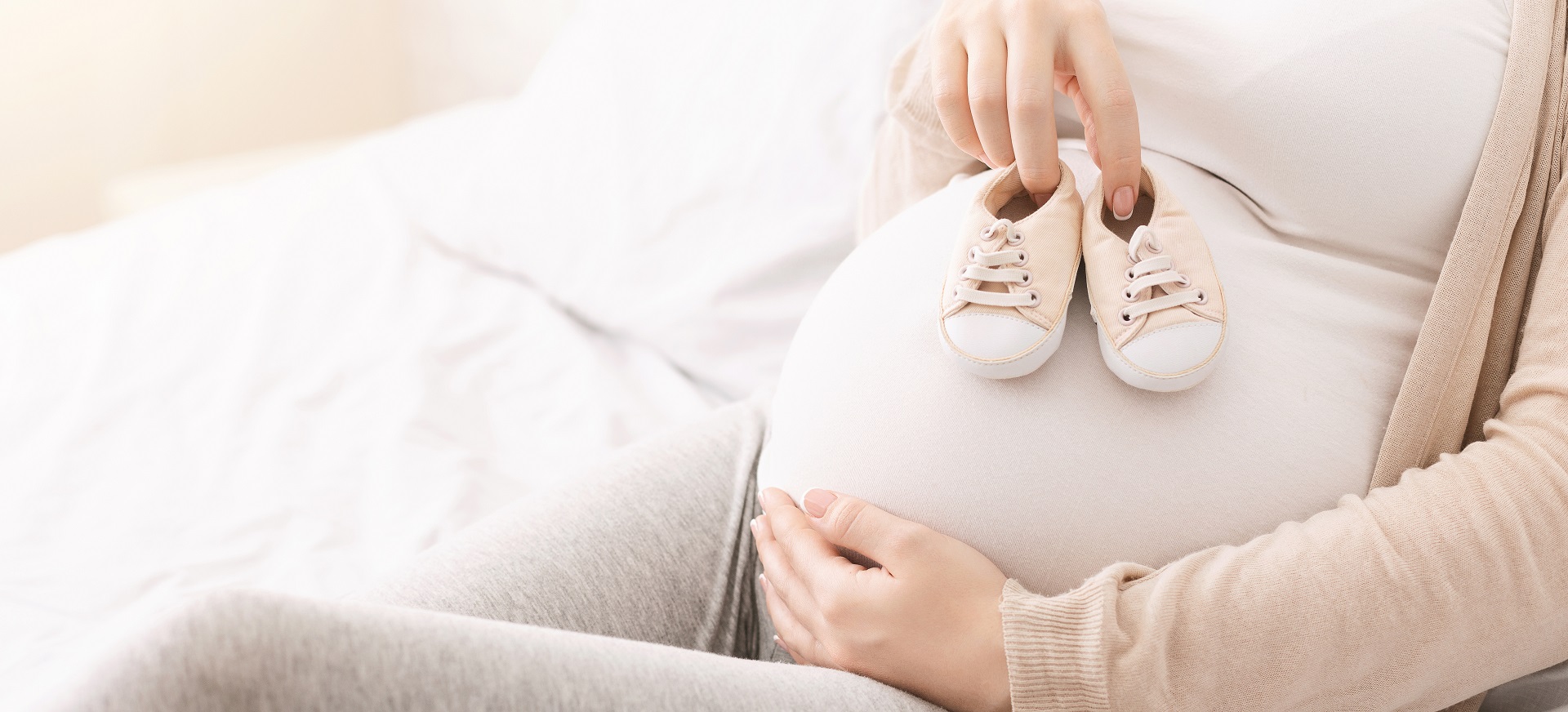 Kobieta w ciąży trzyma niemowlęce buciki na brzuchu