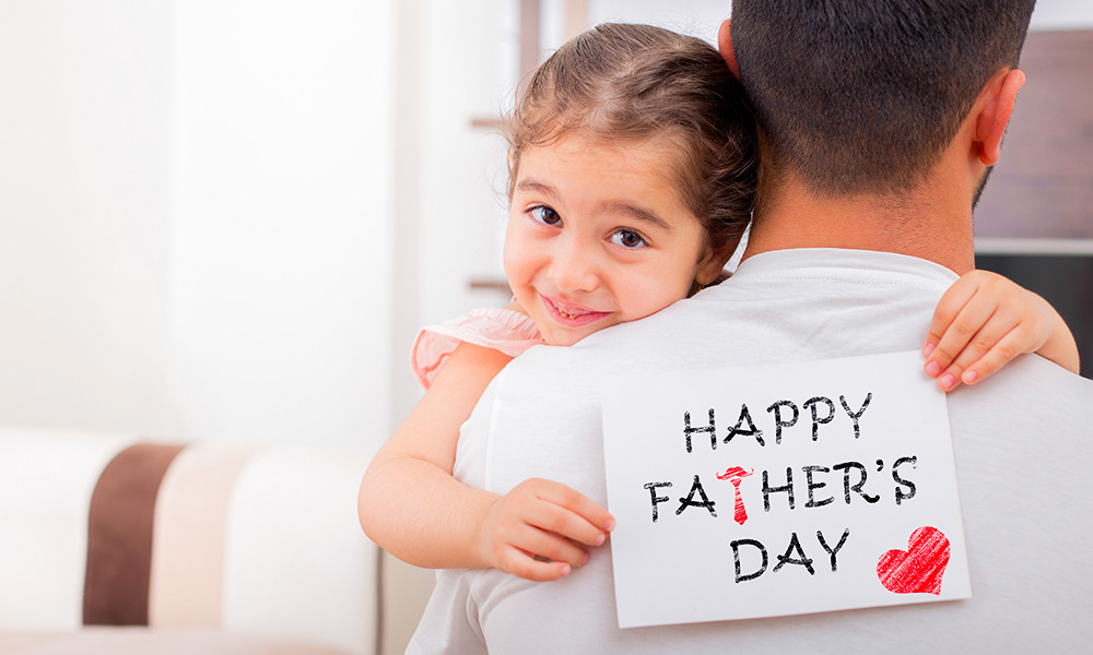 Mała dziewczynka przytula się do taty i trzyma kartkę z okazji Dnia Ojca