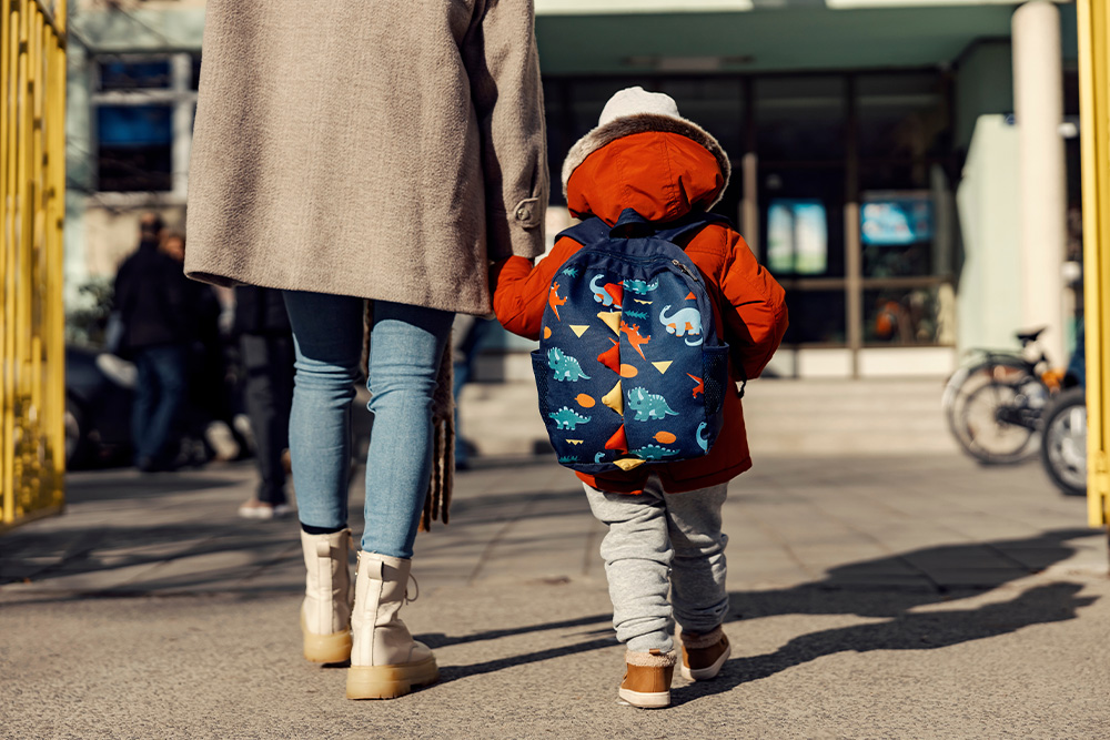 Mama prowadzi za rękę przedszkolaka z plecakiem