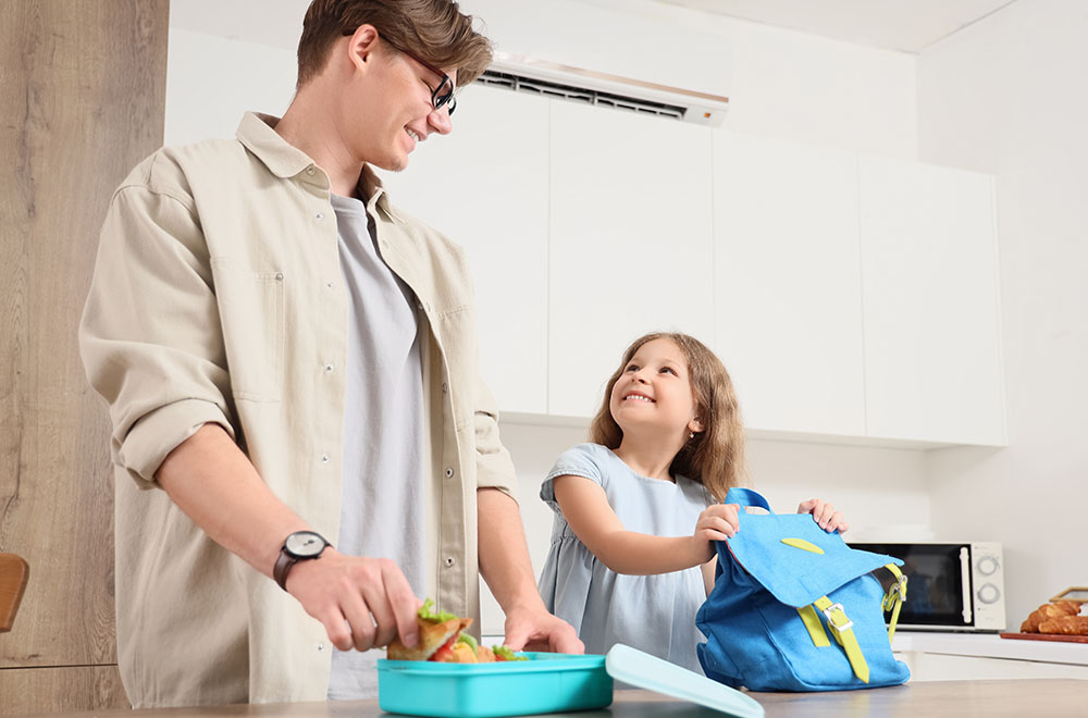 Ojciec przygotowuje lunch dla córki, która uśmiecha się, trzymając plecak. - zdjęcie