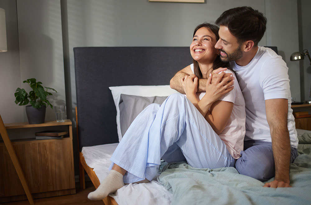 Para śmiejąca się i obejmująca w łóżku, dzieląca się przytulną, radosną chwilą razem. - zdjęcie