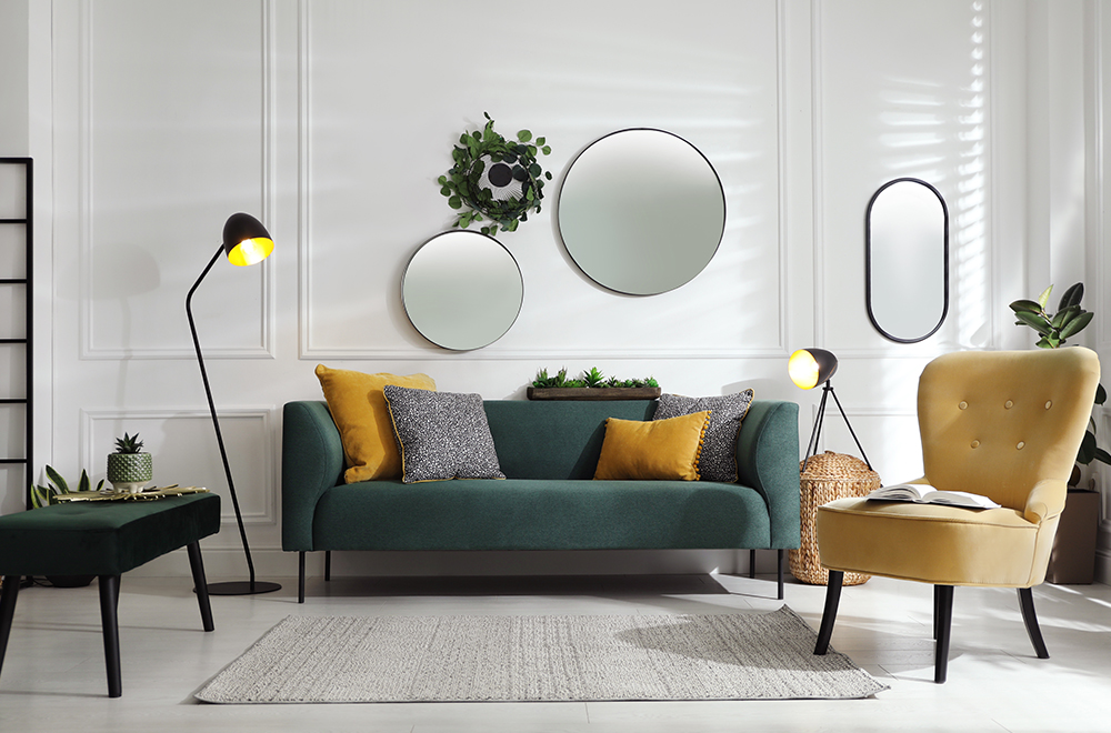 Nowoczesny salon w jasnych kolorach z zieloną sofą, żółtymi poduszkami i okrągłymi lustrami na ścianie. - zdjęcie