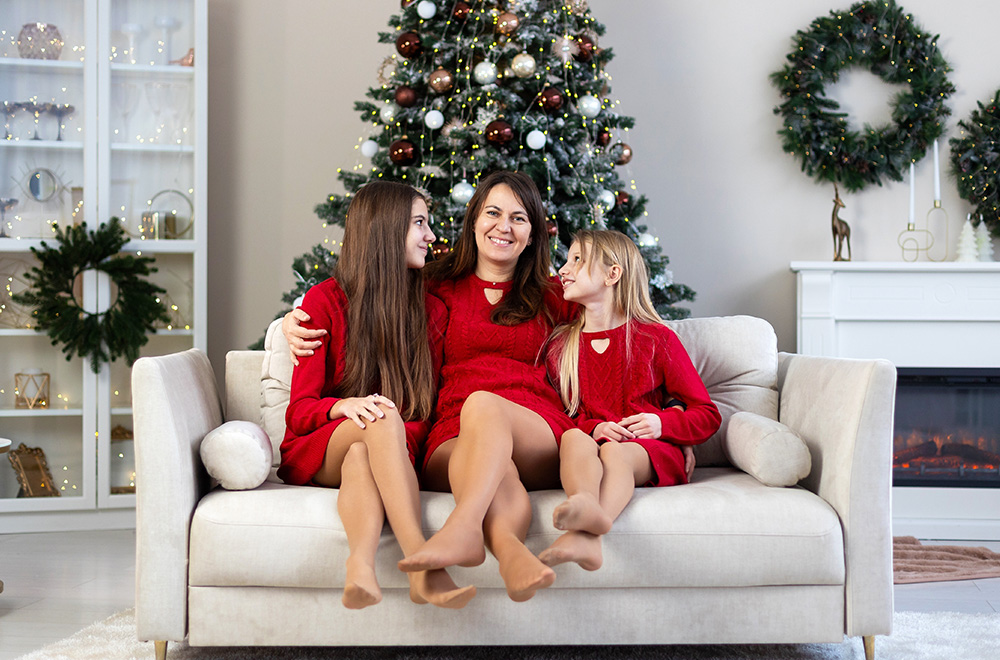 Mama i córki w czerwonych sukienkach spędzają świąteczny czas razem przy choince. - zdjęcie