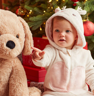 Dziecko w ubranku z reniferem siedzi obok dużego pluszowego psa, a w tle widać choinkę i prezenty. - tytułowa